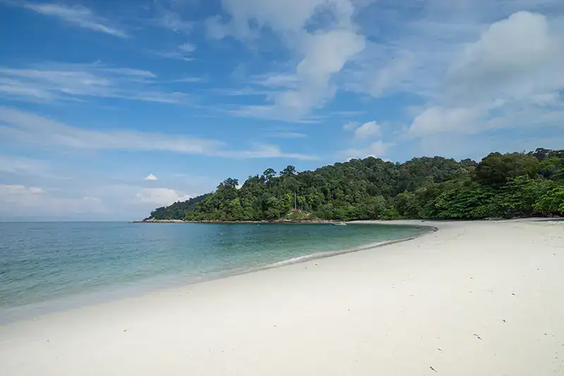 Peaceful view of Teluk Nipah Beach on Pangkor Island with clear turquoise water, white sandy shore, and lush greenery in the background.