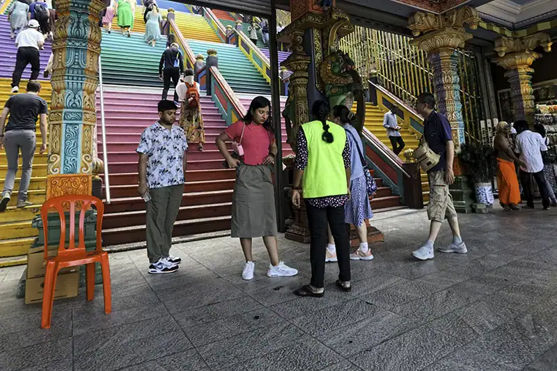 Tourists being stopped at Batu Caves entrance for not following the batu caves dress code, with temple staff advising on proper attire before climbing the colorful staircase.