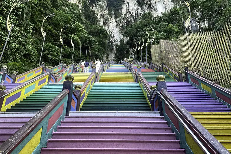 Colorful Batu Caves staircase photographed at 8:00 AM, showing an early morning visit during Batu Caves opening hours with few tourists present.