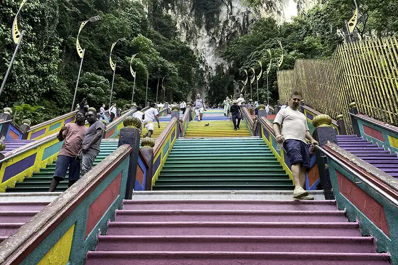 Tourists climbing the colorful Batu Caves staircase at 3:45 PM, highlighting a late afternoon visit during regular Batu Caves opening hours.
