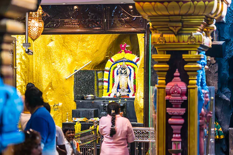 Hindu devotees performing a puja ceremony inside Batu Caves during regular visiting hours, with a golden shrine in the background.