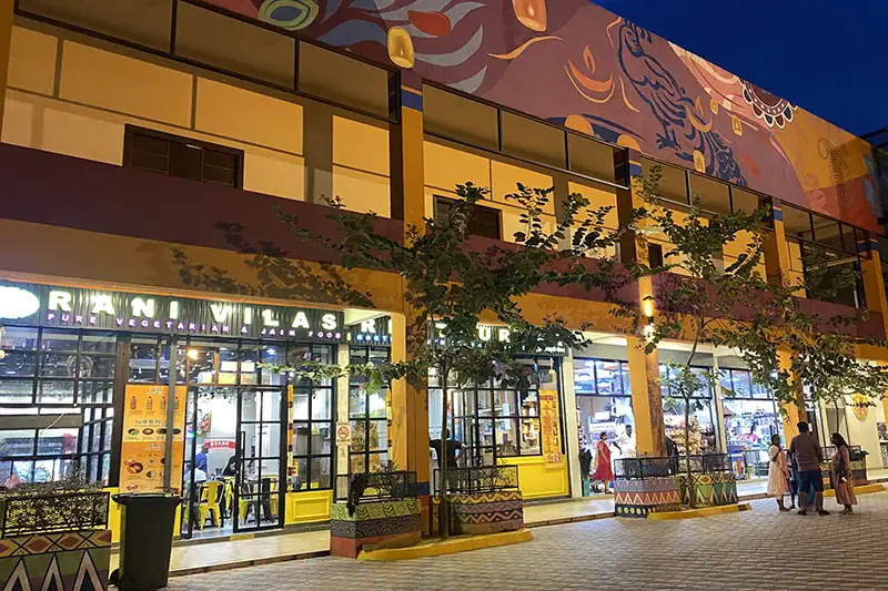 Visitors walking outside a restaurant in Batu Caves complex at 8:00 PM, showing the temple grounds still active during extended Batu Caves visiting hours.