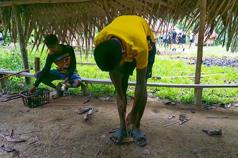 Bateq tribe member demonstrating traditional fire-starting using bamboo and dry leaves in Taman Negara National Park
