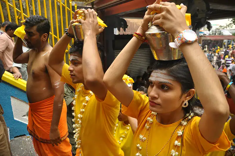Hindu devotees wearing yellow attire and carrying milk pots during Thaipusam at Batu Caves, following the spiritual Thaipusam dress code for Batu Caves Malaysia.