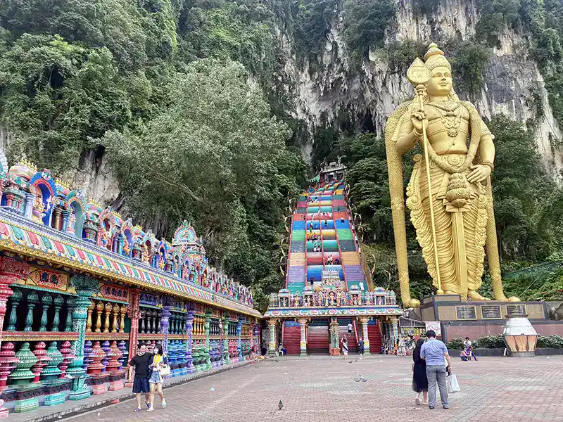 Batu Caves entrance with the golden Lord Murugan statue, rainbow staircase, and colorful Hindu temple — a top attraction in Kuala Lumpur.