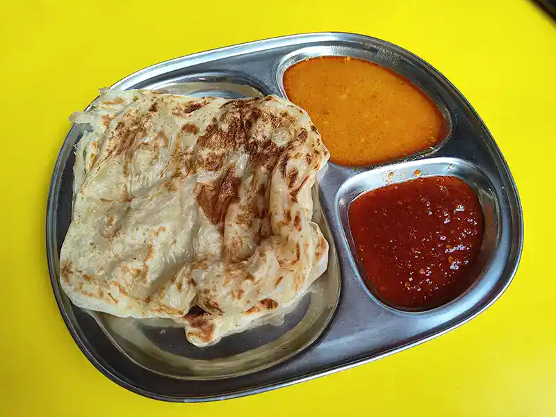 Roti canai served with dhal and sambal, a classic Malaysian food and popular breakfast dish in Kuala Lumpur.