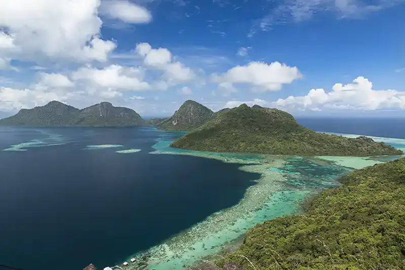 Aerial view of a remote island off the coast of Borneo with shallow reefs and forested hills