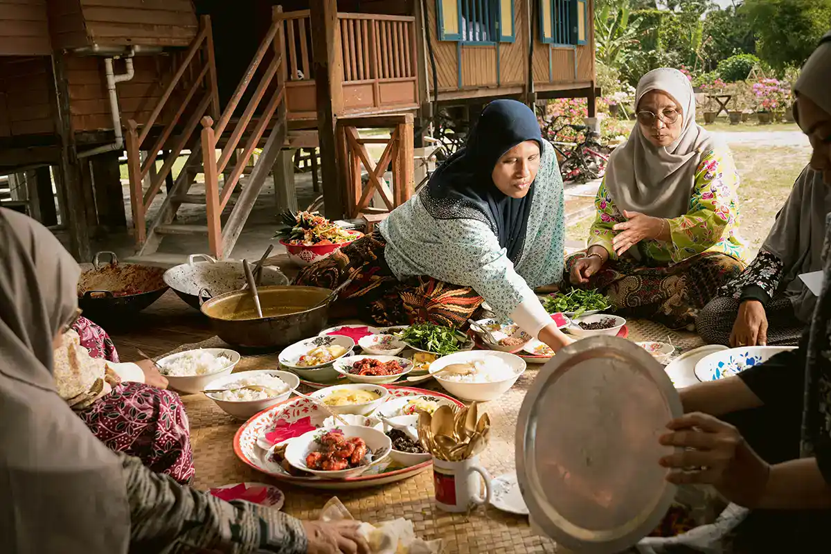 Local women preparing and serving food in a traditional Malay kenduri using dulang trays